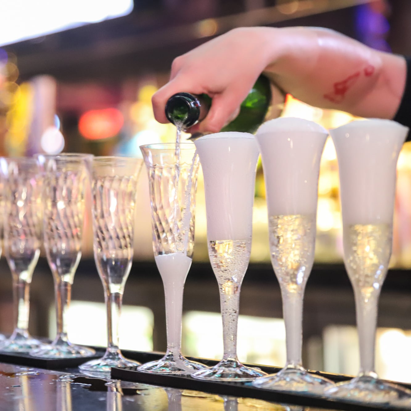 Bartender pouring champagne into a row of glasses on New Year's Eve.