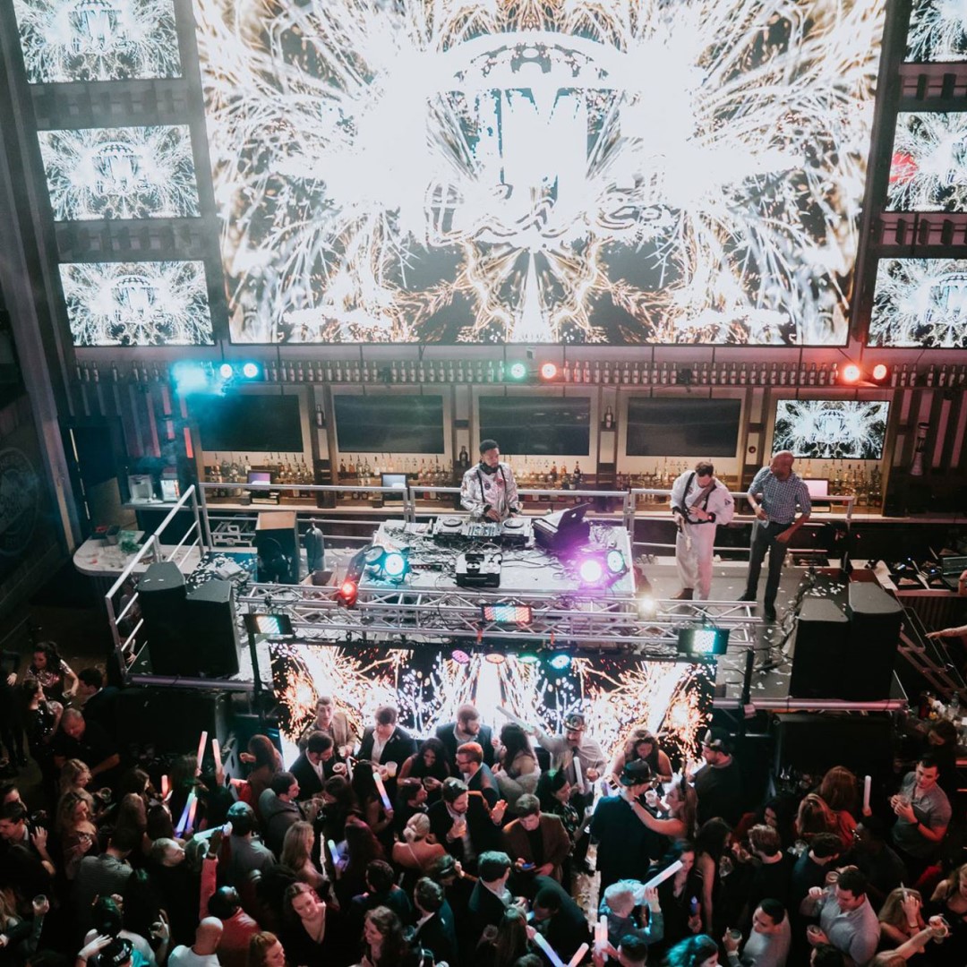 New Year's Eve party with crowded dance floor, DJ, and multimedia wall.